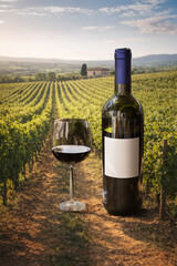 Naklejka premium Red wine bottle and glass standing in vineyard landscape. Concept of wine marketing visuals, luxury alcohol promo, vineyard tourism ads, product branding content, and gourmet lifestyle campaign.