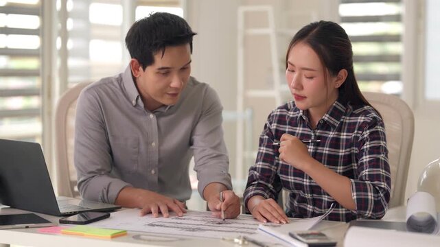 Asian adult architects engineers collaborate design architectural blueprint plans discussing project details review construction drawings modern office workspace
