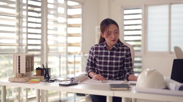 Asian female architect working desk designing building project architectural model office professional engineer drafting blueprint young adult focused concentration interior