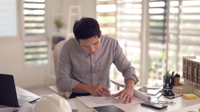 Asian adult male architect drafts architectural blueprints uses ruler pencil construction project design modern office studio workspace