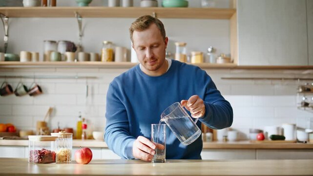 Relaxed guy filling glass with fresh water sitting kitchen interior closeup. 