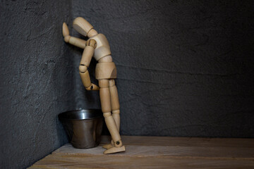 A wooden mannequin stands in the corner, leaning over a metal bowl. Toilet trip concept © алексей мордяшов