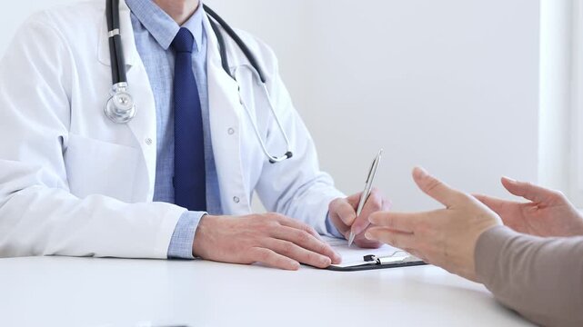 Doctor man taking notes while listening to a female patient explaining her symptoms during a medical consultation in the clinic office. Medicine and health care concept