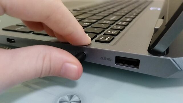 A person inserts a headphone plug into a laptop connector, A hand inserts a wire into the headphone jack on a laptop case.