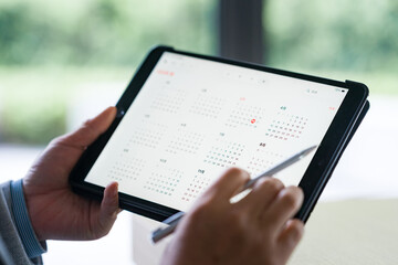 A person holding a tablet and using a stylus to view a digital calendar interface © zhu difeng