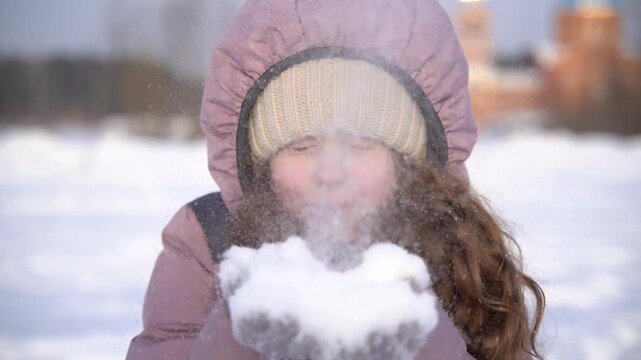 Cute girl blowing a handful of fresh snow toward the camera.