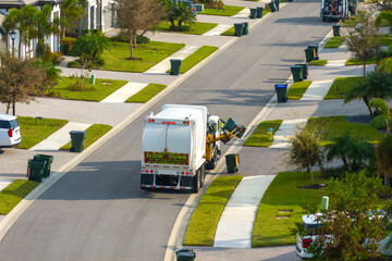 Garbage truck picking up trash bins on suburban street side © bilanol
