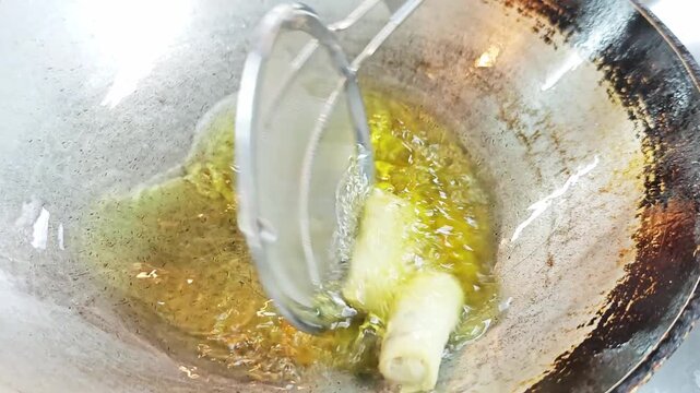 Deep-frying crispy spring rolls in a hot wok with boiling oil.