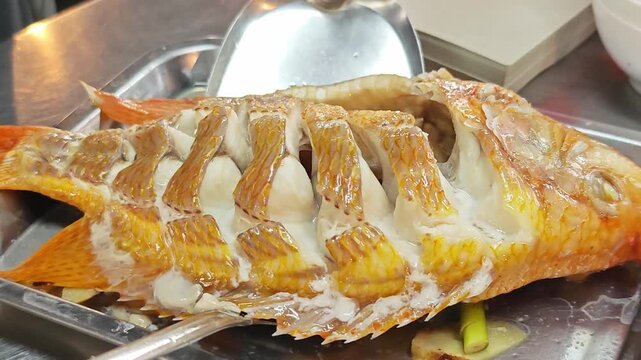Steamed whole red tilapia fish with fresh herbs on a stainless steel tray.