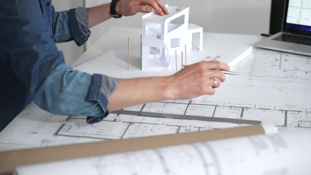 Architect sketching building plans on paper using a ruler and pen while working digitally on a laptop with a blueprint software displaying a floor plan
