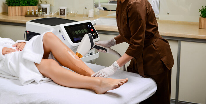Diode laser hair removal procedure on female legs with protective gel. Close up of laser handpiece and specialist hands during epilation treatment