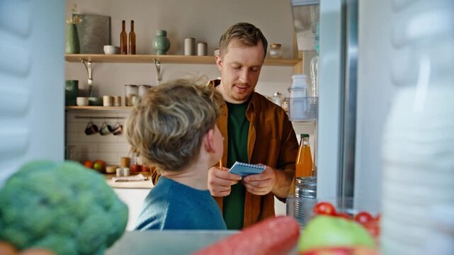 Father son checking fridge planning to buy groceries pov view closeup. Teen boy
