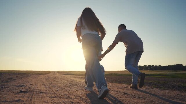 A woman and a man push a bicycle on a dirt path as the woman and man walk under the sun. The dirt path stretches ahead while the bicycle moves forward with the man and woman assist
