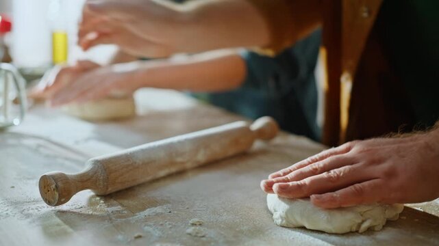 Family hands making dough kneading using rolling pin at home countertop closeup.