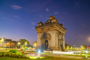 Obraz premium A night view of the Patuxai Victory Monument illuminated against a deep blue sky in Vientiane, Laos, showcasing traditional Lao architecture blended with monumental design in a peaceful 