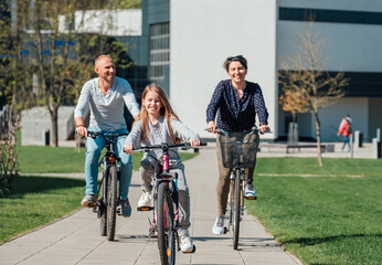Obraz premium Happy family with a young daughter riding bicycles on a paved path in a sunny park as a symbol of active lifestyle and healthy outdoor recreation for parents and children during a family weekend trip