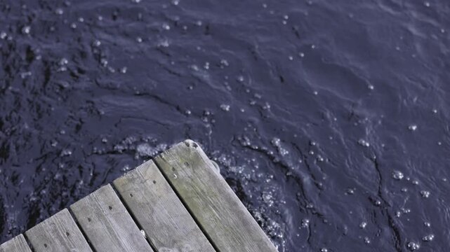 High angle slow motion shot of wooden dock corner over rippling dark blue water with copy space - Finnish spring time