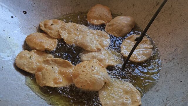 Indian poori puri bread frying in hot oil inside a large wok kadhai. The dough puffs up into golden, crispy pooris during the traditional cooking process. Perfect for showcasing Indian cuisine