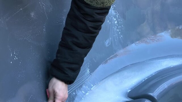 Tub being cleaned with sponge and water by hand in outdoor setting, hygiene concept. bath surface covered with moisture and dirt being removed, tub wall actively scrubbed, maintenance process