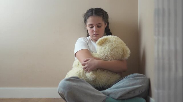 Young girl sitting on the floor with teddy bear. Teddy bear punished by sad corner. Teenage girl is traumatized by a violent attack by a teenager. A young girl is seated on lifestyle the floor with a.