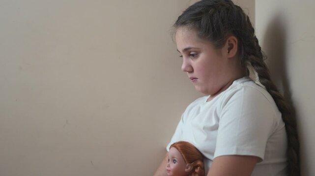 Young girl sitting on the floor with her doll. Girl punished with a doll in a corner. A teenage girl is traumatized by violence and psychological trauma. A young girl lifestyle is on the floor with.