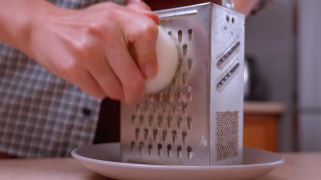 Female hands grating a whole onion or onion for cooking a meal or salad in the kitchen