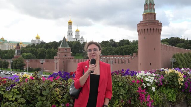 A female journalist transmits news with a microphone in her hands against the background of Red Square and the Kremlin in Moscow