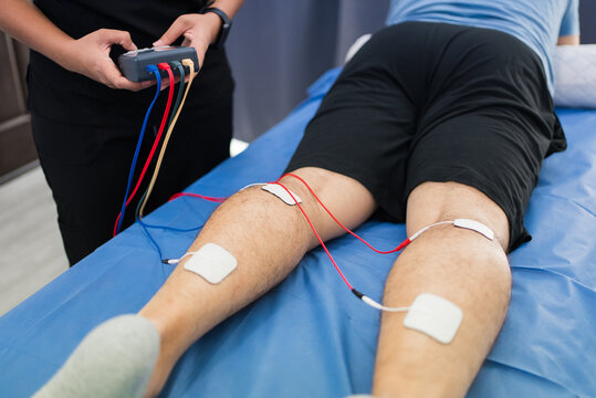 Therapist providing electrical muscle stimulation for leg pain rehabilitation