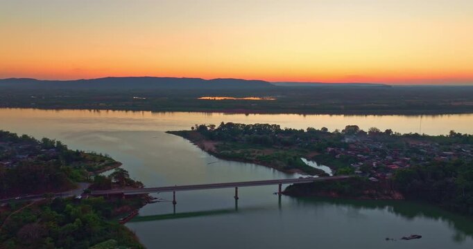 A breathtaking aerial view of sunset casting golden light over the Nam Kading River and Pak Kading Bridge, creating vivid reflections and a peaceful evening atmosphere in central Laos.