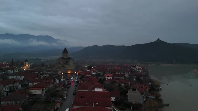Aerial view of mtskheta, georgia, at dusk with svetitskhoveli cathedral, jvari monastery on the mountain, and the mtkvari river under a cloudy, gloomy sky