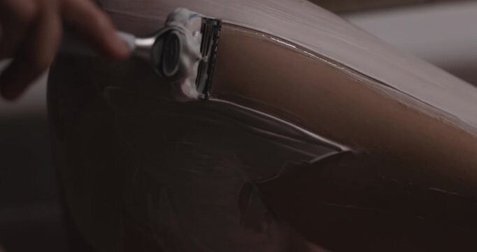 Woman shaves her leg with a razor while lying in the bath with red water