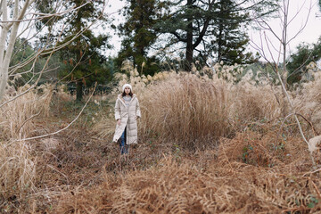 Naklejka premium Winter scene with a lone person in a light coat standing among tall dried grasses in an open field, calm and natural, highlighting solitude and outdoor exploration.
