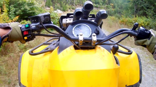 Man wearing helmet driving an ATV on a forest road, with bumping into small rocks and scattering them along the path. Close up shot of the yellow ATV and the speedometer from the rider's point of view