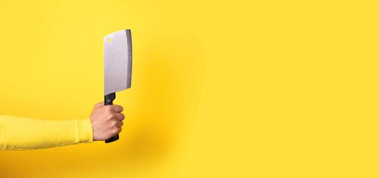 Close-up of a hand gripping a meat cleaver against a bright yellow background, ideal for culinary, cooking, or kitchen-related concepts.