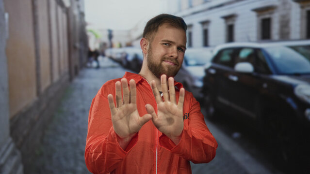 Man prisoner in orange jumpsuit holding palms forward on street with visible inmate number 382586 and beard; defiance isolation.