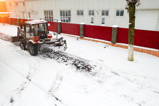 red snow plow tractor clears sidewalks rear view.
