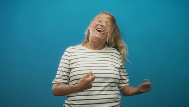 Senior woman with striped shirt, mouth open and hair whipping as she air guitars and headbanging in studio; joy.