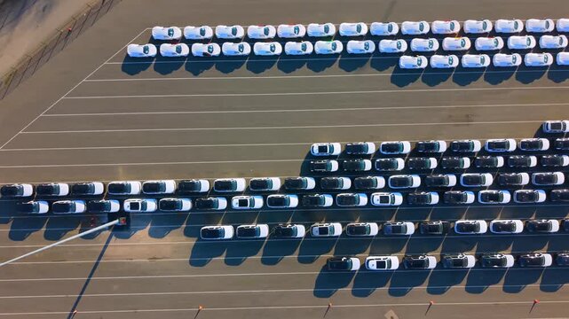 Vertical aerial video showing rows of new imported vehicles, some in protective white covers, parked at the Seaforth automotive terminal in UK. 