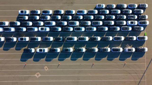 Vertical aerial video showing rows of new imported vehicles, some in protective white covers, parked at the Seaforth automotive terminal in UK. 