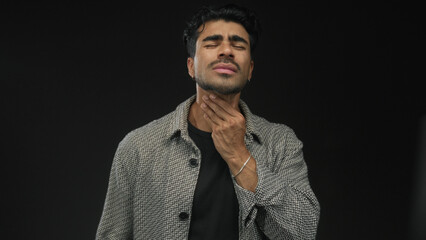 Fototapeta premium Young hispanic man hand on neck with pained expression in studio with black backdrop; discomfort.