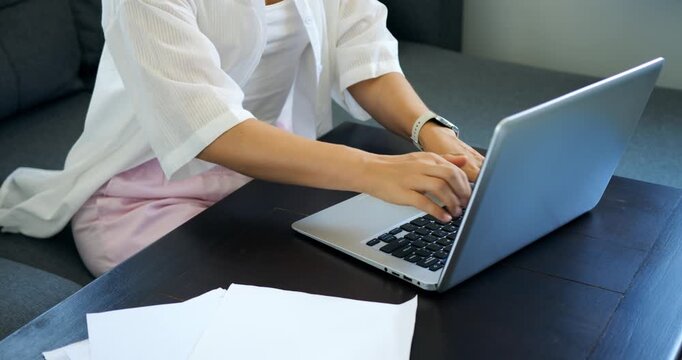 Female individual manages multiple tasks. Woman organizes papers while working at home. Individual diligently multitasks at laptop surrounded by documents in relaxed home office setting