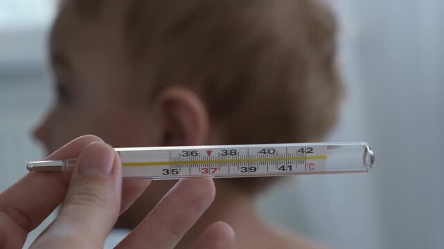 A mercury or alcohol thermometer against the background of a small child, a concept of illness, flu, or high fever in a small child