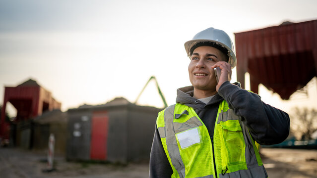 Young engineer, male, using a smartphone while wearing protective gear on a construction site