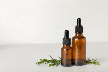 Fototapeta premium Rosemary essential oil on a textured background. Rosemary essential oil with fresh leaves nearby. Green rosemary sprig. Natural medicine, organic hair product, skin care, spa therapy. Beauty concept. 