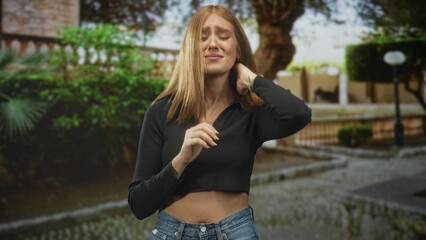 Fototapeta premium Woman with hands clasped near chest showing midriff in a courtyard building; yearning introspection.