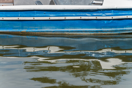 Blaue Seite eines Ruderbootes (Detail) in einem Freizeitpark, das sich im Wasser spiegelt