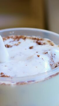 Cream extends smoothly. Silky foam stretches gracefully inward. Closeup reveals glossy foam being pulled into long strip. Detailed view of soft cream elongating over cup with straw
