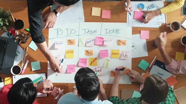 Top down aerial view of diverse business team making scrum task board at meeting room. Group of smart people writing at paper and sticky notes for making kanban board to manage work flow. Convocation.
