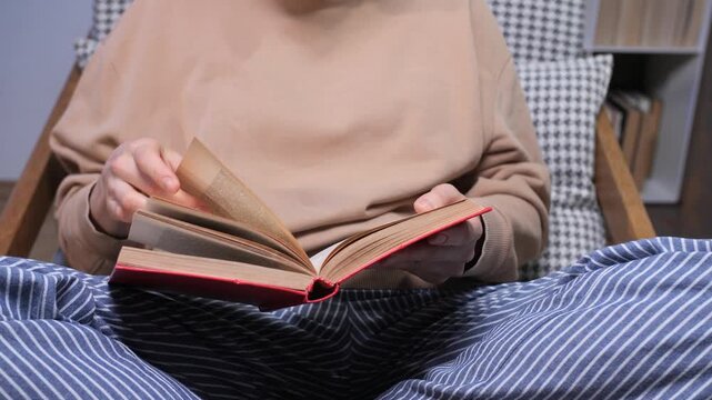 Person sits cozily in an armchair at home, turning pages of a book, enjoying quiet, screen free reading time and peaceful relaxation for learning and self care