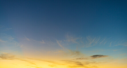 Naklejka premium Beautiful Golden Sunset Sky with Wispy Orange Clouds,A wide-angle shot of a stunning sunset sky featuring vibrant yellow and orange clouds scattered across a deep blue and purple gradient background d